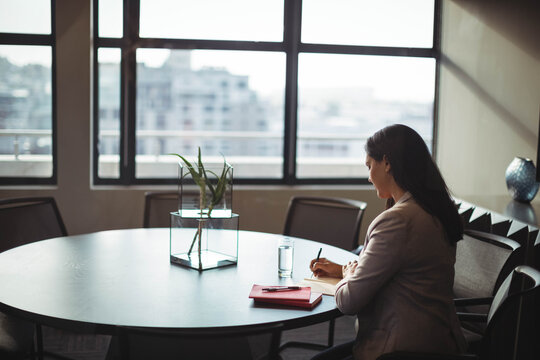Round conference table featuring glass terrarium, red folder, pen and water glass in meeting room - Powered by Adobe