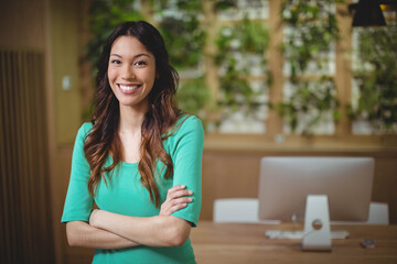 Female office professional smiling while crossing arms at desk with plant wall, copy space