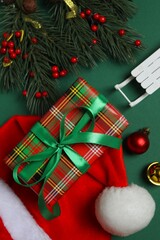Top view of gift boxes tied with bow, santa hat and Christmas decorations on green background 