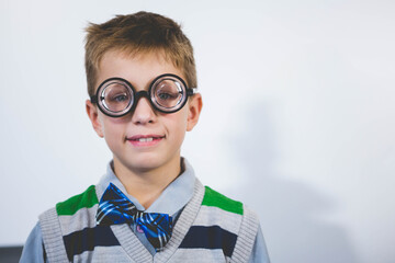 School-age boy posing against studio wall wearing striped sweater vest novelty glasses and bow tie