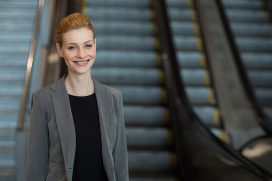 Businesswoman standing and smiling in lobby near escalators with metal handrails, copy space - Powered by Adobe