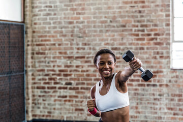 African American woman punching with dumbbell and pink wrist wrap in fitness studio
