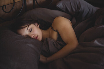 Sleeping Asian woman lying on side in bedroom by wrought iron headboard with dark gray bedding