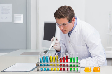 Adult male scientist using pipette depositing liquid into test tube rack on lab bench with flasks