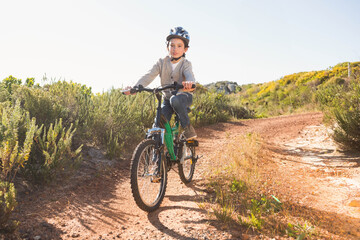Boy wearing safety helmet riding green mountain bike on rural dirt trail under bright sunlight
