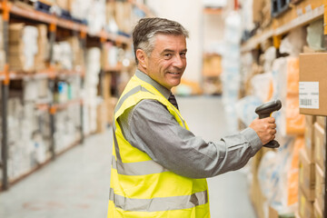 Male warehouse worker scanning boxes with handheld barcode scanner inside aisle wearing safety vest