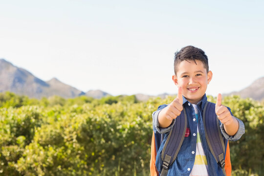 Fototapeta Boy standing outdoors in countryside giving thumbs up wearing denim shirt and backpack, copy space