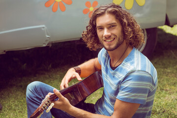 acoustic guitar is resting on green grass in front of retro camper van, with flower graphics