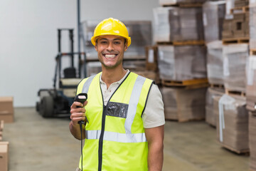 Male warehouse worker in yellow helmet and neon vest scanning boxes with barcode scanner in storage