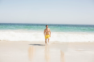 Man running up wet sandy shoreline at beach wearing yellow swim trunks with turquoise water waves