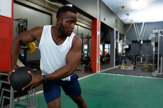 Fototapeta Muscular athlete twisting torso with black medicine ball on green turf in modern gym, copy space