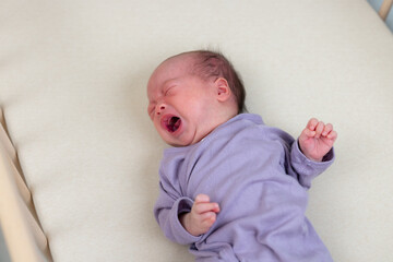 Newborn baby crying loudly while lying on bed