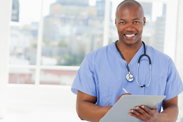 African American male doctor writing notes on clipboard with stethoscope in clinic room, copy space