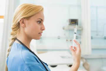 Female medical professional inspecting syringe in clinic with stethoscope near bed, copy space