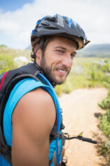 Male mountain biker standing on dirt trail glancing back wearing helmet and hydration pack