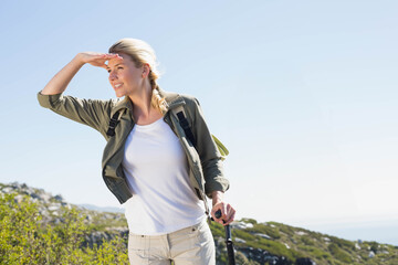 Woman shading eyes scanning horizon on rocky hillside with trekking pole and backpack, copy space