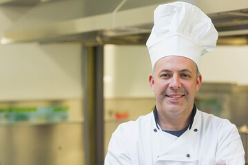 Male chef wearing white chef jacket and hat standing under vent hood in kitchen, copy space
