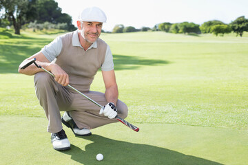 Senior male golfer in golf attire lining up putt on putting green with golf ball