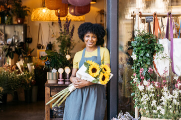 Young florist owner smiling and holding a bouquet of sunflowers in her flower shop