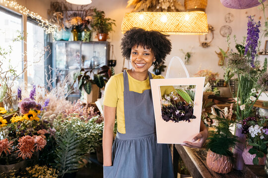 Florist owner smiling and holding a bouquet in her flower shop, surrounded by colorful flowers and plants