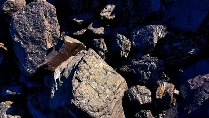 A close-up of large, rugged rocks with rough textures and dark shadows, illuminated by natural light, highlighting their uneven surfaces and natural formations