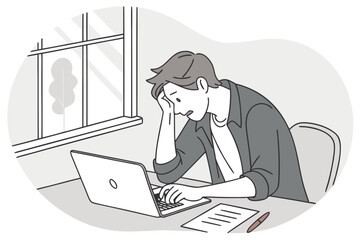 Frustrated young man working on laptop while sitting at desk next to window during daytime