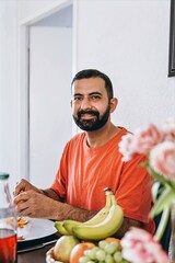 Middle Eastern man with dark hair and beard sitting at breakfast table,peeling a tangerine and...