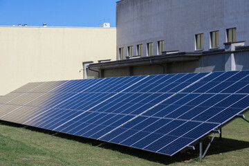 Expansive blue solar panel array on green grass by modern industrial buildings, efficiently generating clean renewable energy for sustainable enterprise power needs