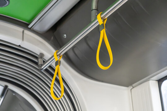 Modern public transit interior showcases a shining chrome handrail with vibrant yellow hanging handles, essential for passenger safety and urban convenience - Powered by Adobe
