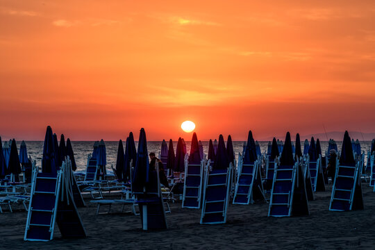 ombrelloni al tramonto 01 - sole basso sull'orizzonte con cielo rosso e ombrelloni chiusi sulla spiaggia.