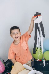 Smiling little boy proudly shows his handmade pirate craft in a cozy playroom, surrounded by toys...