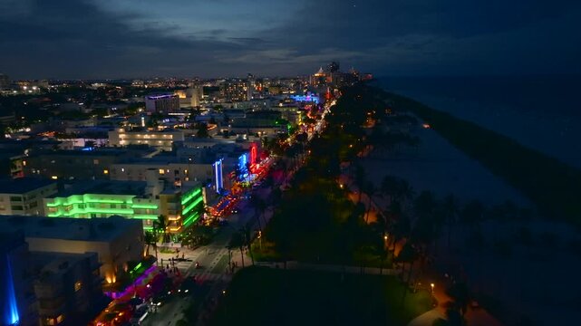 Aerial view of Ocean Drive shows vibrant neon lights illuminating the street and buildings contrasting with the dark ocean and sky, Miami Beach, Florida, United States.