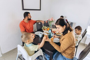 Young family having breakfast together. Parents and kids at the table in a realistic morning scene...