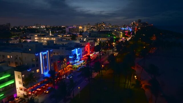 Aerial view of colorful buildings along Ocean Drive, illuminated by vibrant neon lights at night, casting a warm glow on the street, Miami Beach, Florida, United States.