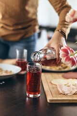 Close-up of a glass as a woman pours red fruit juice or compote from a bottle. Morning breakfast...