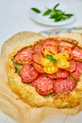 A delicious tomato galette is displayed on parchment paper, showcasing layers of vibrant red and yellow tomatoes atop a flaky crust in a warm kitchen atmosphere.