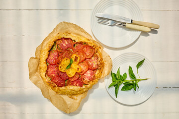 A delicious tomato galette is displayed on parchment paper, showcasing layers of vibrant red and...