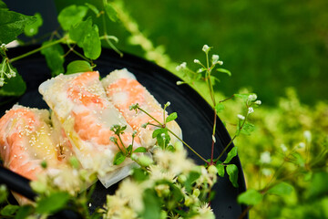 Colorful spring rolls filled with vegetables and shrimp are arranged on a dark, round tray. Lush...