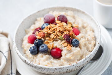 Oatmeal porridge with berries and granola topping served in ceramic bowl, closeup view. Healthy vegan breakfast meal, for diet, weight loss and healthy lifestyle
