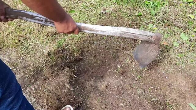 man cleaning the edge of an asphalt road using a hoe during a communal work. clearing soil and grass covering the roadside