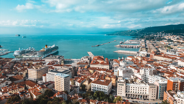 Aerial view of the vibrant cityscape meeting the tranquil sea, dotted with ships and the iconic port, a tapestry of terracotta roofs and modern structures, Trieste, Friuli-Venezia Giulia, Italy.