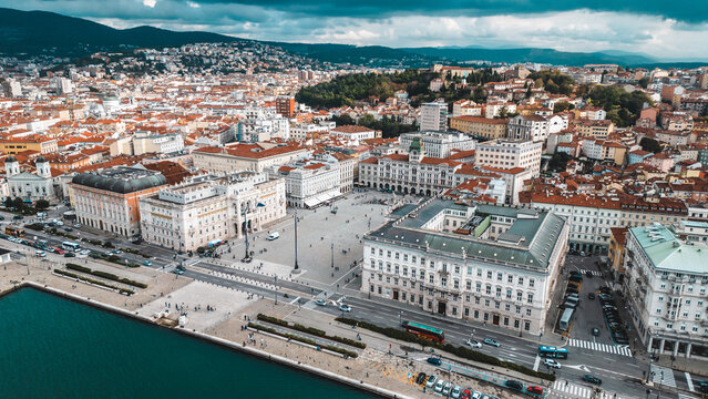 Aerial view of the Piazza Unit&Atilde;&nbsp; d'Italia's grand architecture meets the Adriatic's turquoise embrace, framed by terracotta rooftops and verdant hills, Trieste, Friuli-Venezia Giulia, Italy.