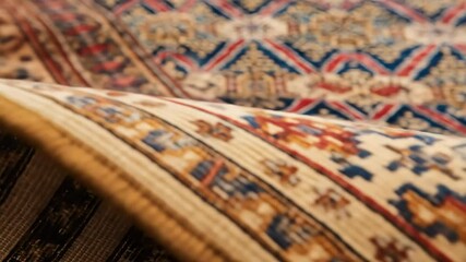 A macro shot pans over a rolled-up, ornate rug, revealing its intricate weave, texture, and colorful traditional pattern - Powered by Adobe