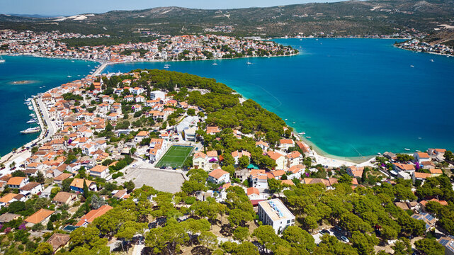 Aerial view of a peninsula with terracotta rooftops meeting the turquoise sea, connected by a bridge to the mainland, Rogoznica, &Aring;&nbsp;ibensko-kninska &Aring;&frac34;upanija, Croatia.