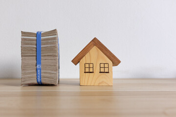 Stack of Cash and Wooden House Miniature on Wooden Surface