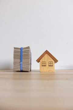 Stack of Cash and Wooden House Miniature on Wooden Surface