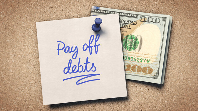 Pay off debts - A sticky note with 'Pay off debts' written in blue ink is pinned to a corkboard with a blue pushpin