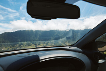 Scenic mountain landscape view from a car's windshield on a bright, cloudy day, emphasizing road...