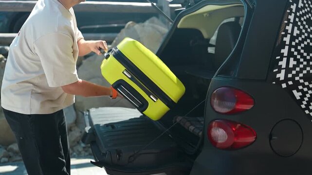 Traveler loading bright yellow suitcase into the trunk of a small black car Preparing for a trip or vacation Compact urban vehicle and travel gear under daylight Perfect theme for transport mobility