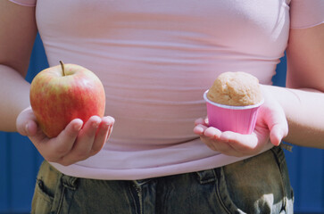 a girl holding an apple in one hand and a cake in the other, a weight loss concept